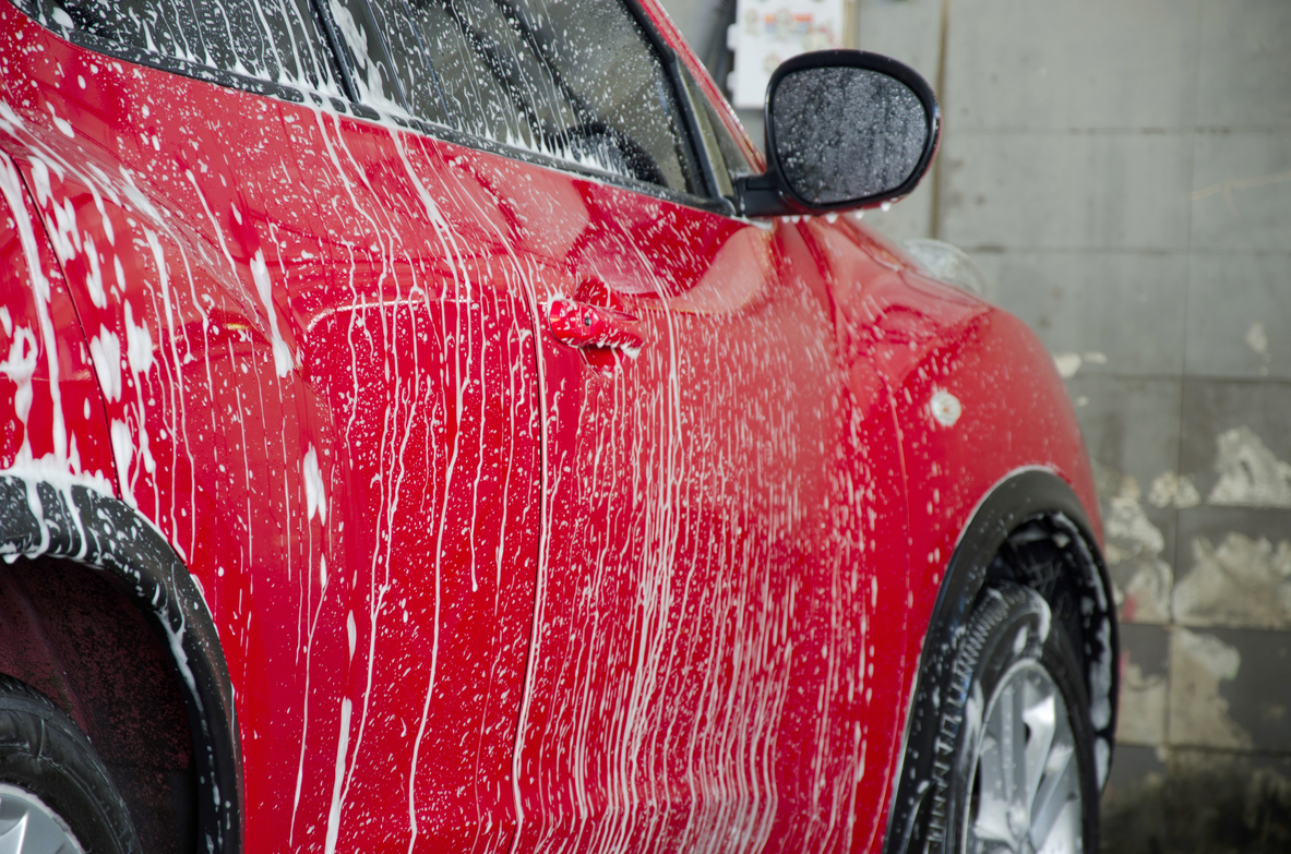 Red car with foam in car wash to illustrate car detailing Portland.